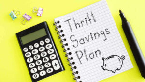 A calculator and pen are pictured next to a notepad with the words 'Thrift Savings Plan' written on it against a yellow background